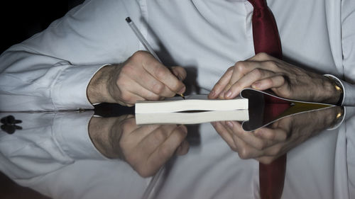 Midsection of businessman writing in book on glass table