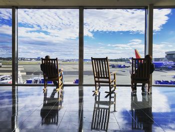 Chairs and tables against sky seen through glass window