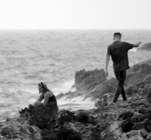 Man standing on rock by sea against sky