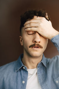 Tired young man with head in hand against brown background