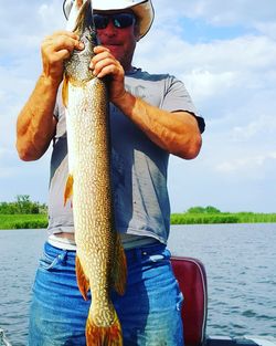 Portrait of man holding fish in lake against sky