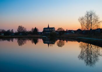 Scenic view of lake by buildings against sky during sunset