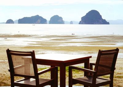 Chairs and table on beach against sky