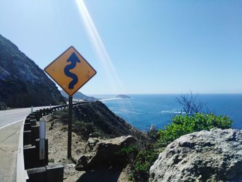 Road sign by sea against clear blue sky
