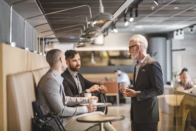 Senior businessman talking with male coworkers during coffee break in office