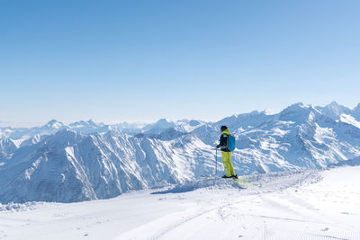 Woman hiking on snowcapped mountain peak while looking at landscape against sky