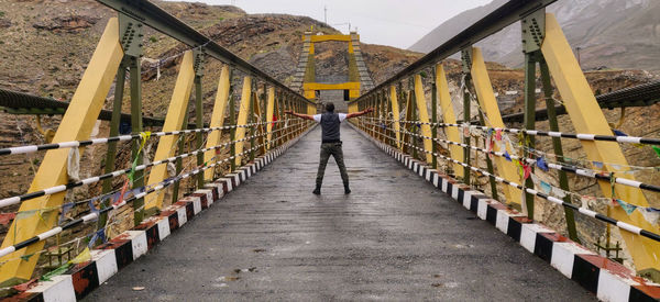 Person standing on a high altitude suspension bridge with open arms. 