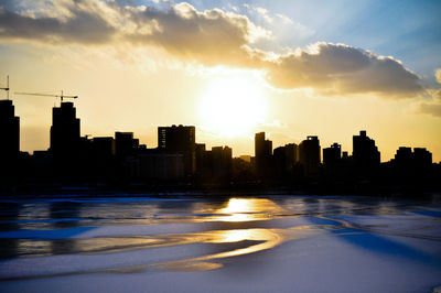 Silhouette city by sea against sky during sunset