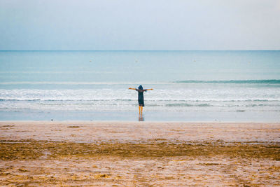 Rear view of man standing at beach against sky