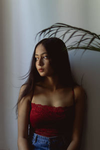 Portrait of young woman looking away against wall