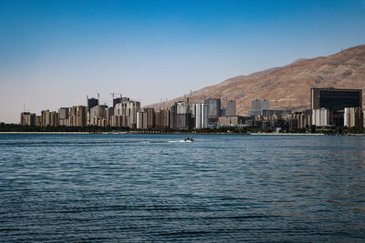 Scenic view of sea by buildings against clear blue sky