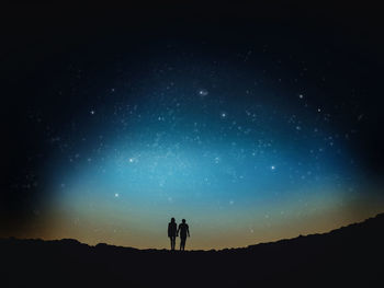 Low angle view of silhouette man and woman walking on field against sky at night