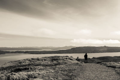 Silhouette person standing by river against cloudy sky at dusk