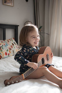 Happy girl playing guitar on bed at home