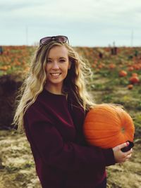 Portrait of smiling young woman holding pumpkin standing in field