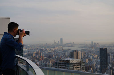 Man photographing cityscape against sky in city during sunset