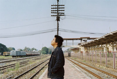 Side view of man standing at railroad station against sky