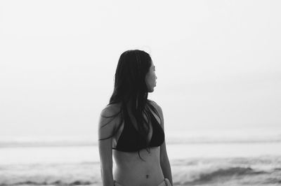 Woman in bikini standing at beach against sky