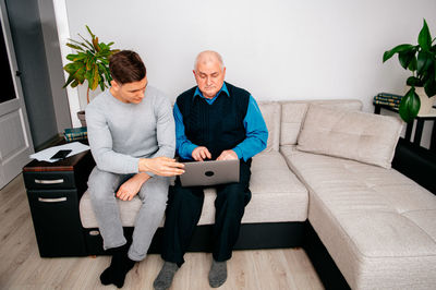 Smiling man using laptop sitting with grandfather at home