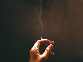 Human hand holding cigarette against black background