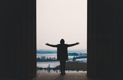 Rear view of silhouette man standing by sea against sky