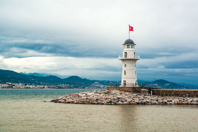 Turkish flag on lighthouse by sea against cloudy sky