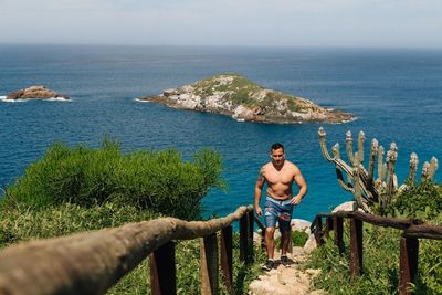 Full length of shirtless man in sea against sky
