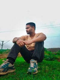 Young man looking away while sitting on field