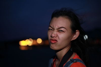 Portrait of young woman making face against sky at night
