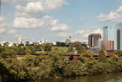 Trees and buildings in richmond against sky near the james river.