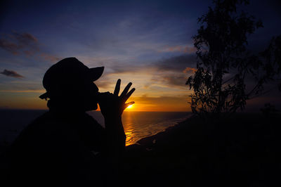 Silhouette man holding sun against sky during sunset
