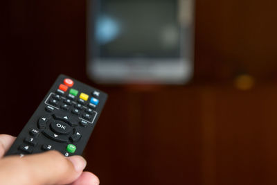 Cropped hand of person holding remote control while watching tv