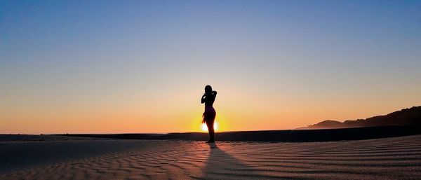 Silhouette woman standing at beach against clear sky during sunset