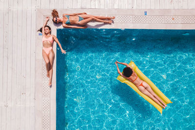 Directly above shot of females wearing bikini lying on inflatable ring