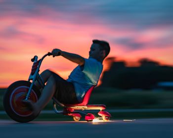 Boy riding motorcycle against sky during sunset