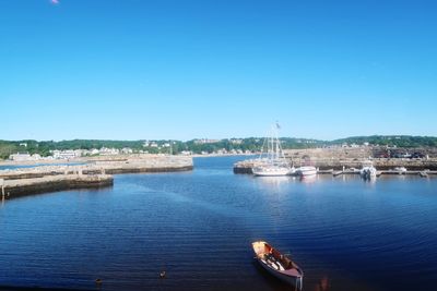 Boats sailing in river against clear blue sky