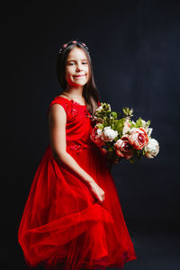 Portrait of girl in dress holding bouquet while standing against black background