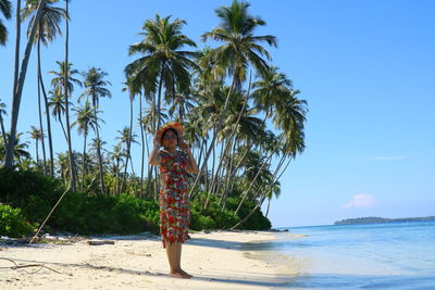 Person standing by palm tree on beach against sky