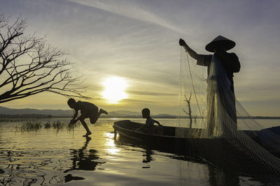 Silhouette men standing on boat against sky during sunset