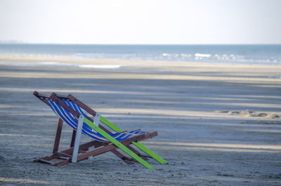 Deck chairs on beach against sky