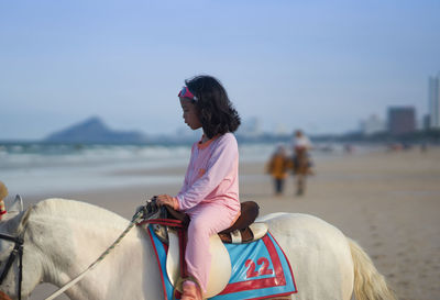 Cute girl sitting on horse at beach