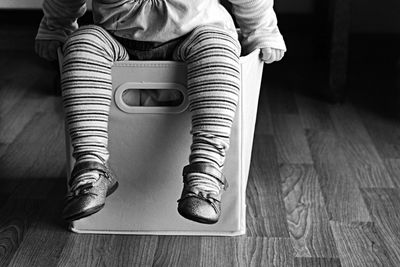 Low section of girl sitting in shopping bag on hardwood floor