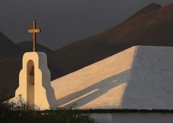 Shadow of church cross on building by mountain against sky