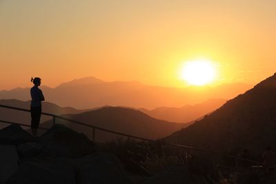 Silhouette woman standing on cliff at sunset