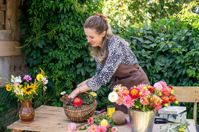 Cute florist girl collects a bouquet of autumn flowers in a basket on the table