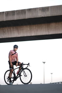 Low angle view of man with bicycle against bridge