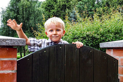 Portrait of cute boy standing by gate against trees