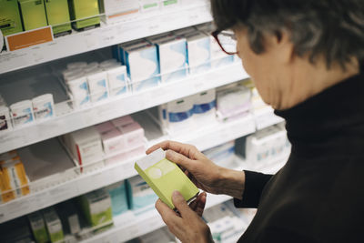 High angle view of senior female customer examining medicine by rack at pharmacy store