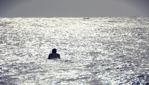 Rear view of silhouette man in sea against clear sky