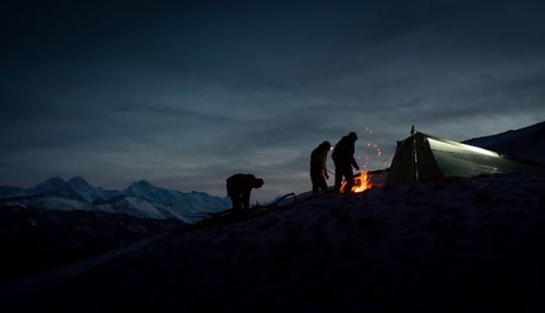 People standing by bonfire on snow covered mountain against sky